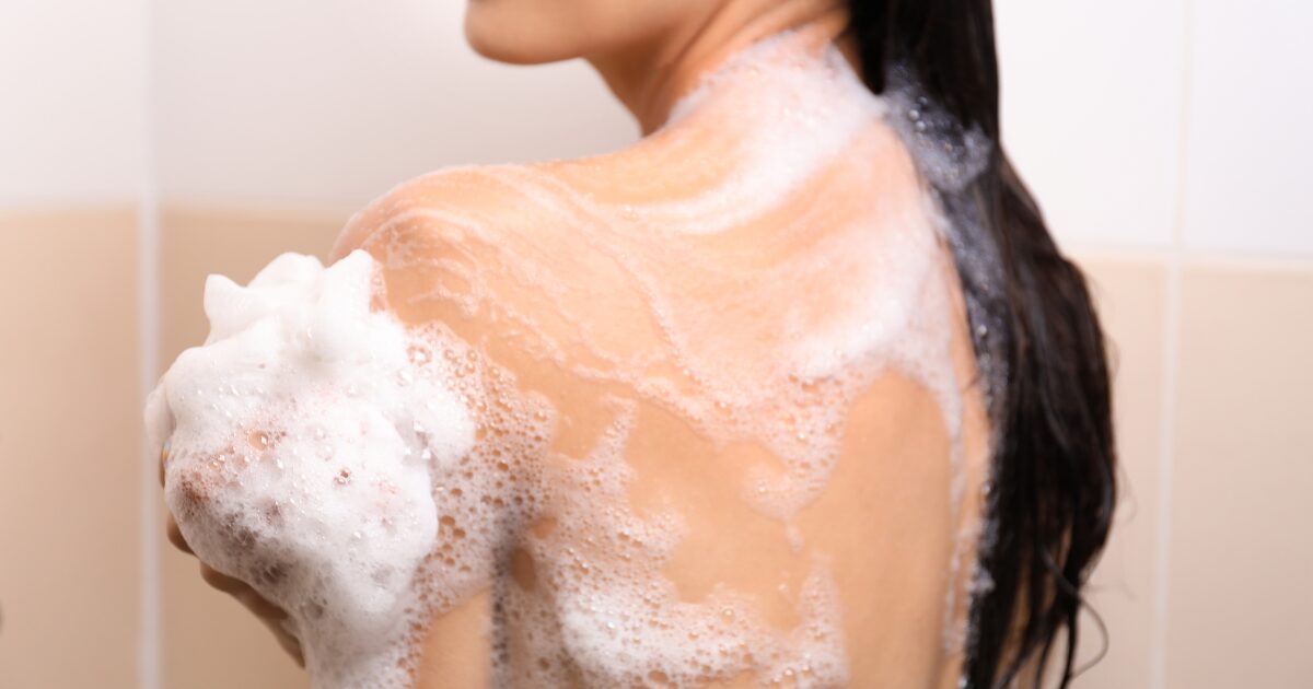 背中ニキビに悩む女性が背中ニキビを治すために、抗真菌成分であるミコナゾール硝酸塩配合のコラージュフルフル 泡石鹸で身体を洗っているイメージ写真。